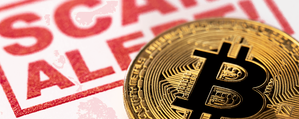 Zbliżenie złotej monety Bitcoin umieszczonej przed czerwonym ostrzeżeniem, na którym dużymi literami widnieje napis „ALERT O OSZUSTWIE”. Tło jest lekko rozmyte, co podkreśla komunikat ostrzegawczy.