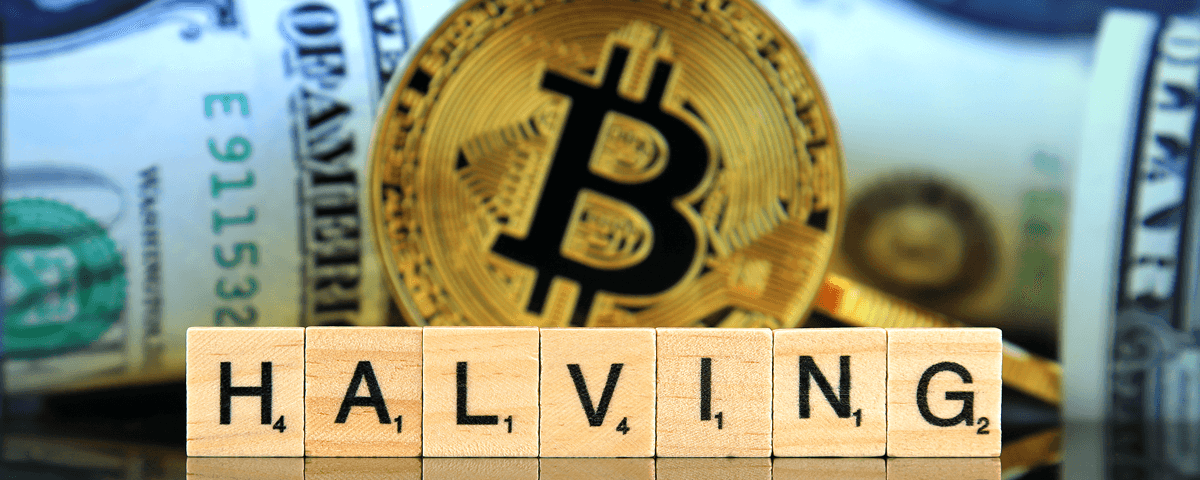 Scrabble tiles spelling "HALVING" in front of a gold Bitcoin symbol and blurred U.S. dollar bills in the background.